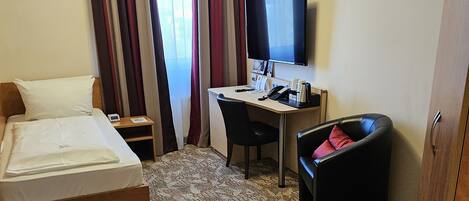 A hotel room with a bed, a desk, a chair, a TV, and a wardrobe.