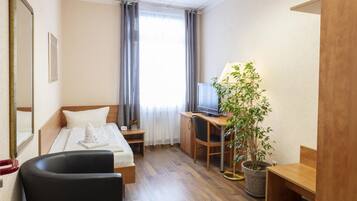 Une chambre d’hôtel avec un lit, un bureau avec un ordinateur, une chaise, une plante en pot et une fenêtre avec des rideaux.