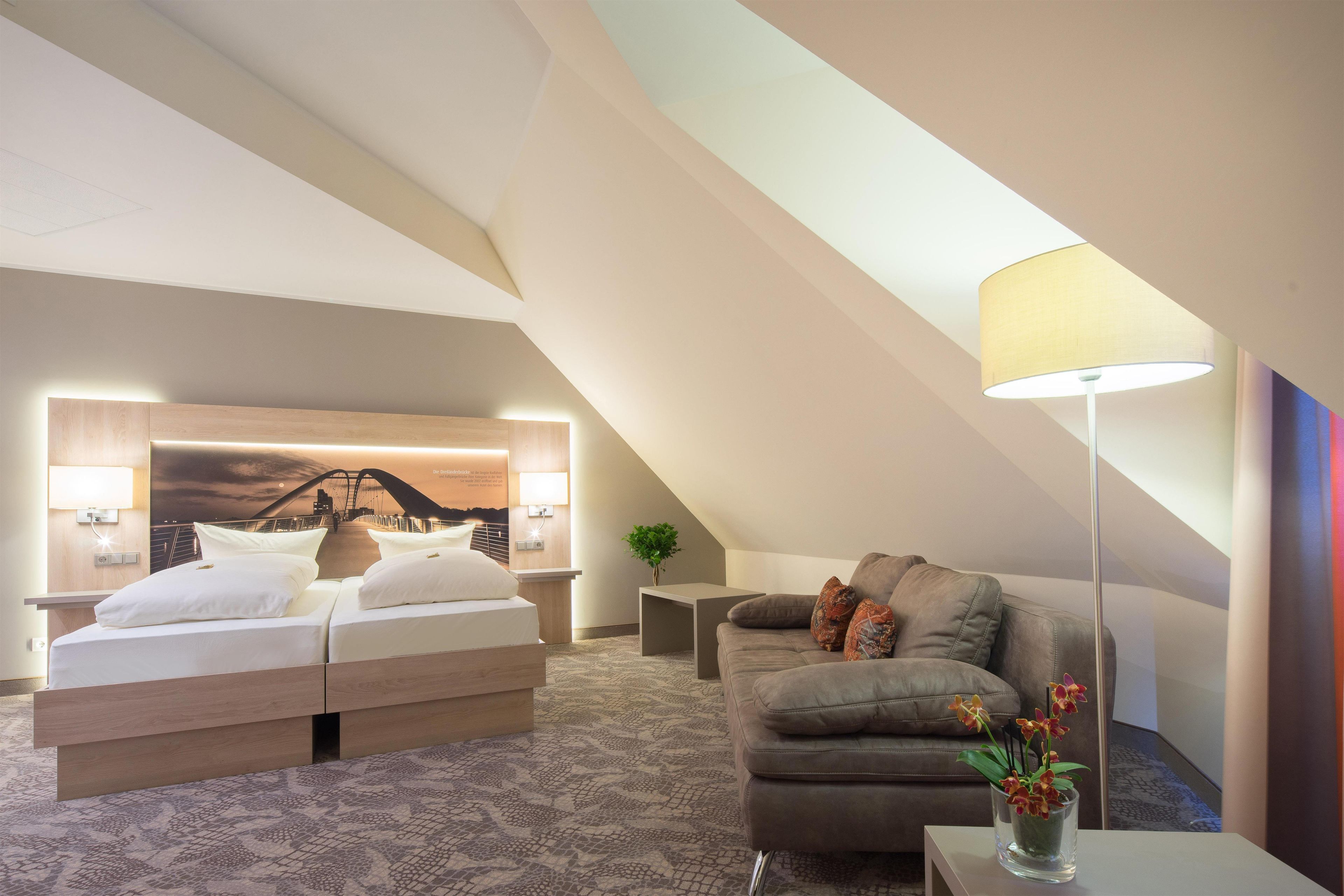 Quarto de hotel moderno com uma cama, um sofá, uma luminária e vista para uma ponte.
