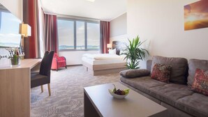 Una habitación de hotel moderna con cama, sofá, escritorio y un amplio ventanal con vistas a la ciudad.