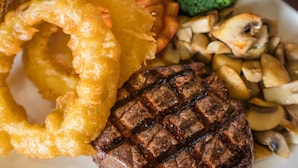 A plate with grilled steak, onion rings, and vegetables. - The Clachan Inn (Drymen)