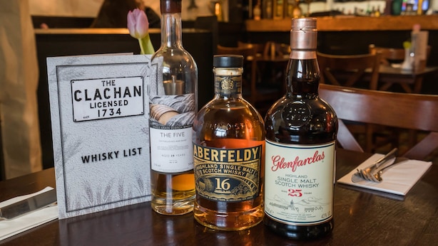 A bar setting with a whisky list sign, bottles of Aberfeldy and Glenfarclas whisky, and a rose. - The Clachan Inn (Drymen)