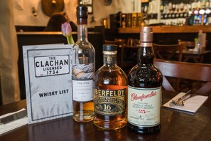 A bar setting with a whisky list sign, bottles of Aberfeldy and Glenfarclas whisky, and a rose. - The Clachan Inn (Drymen)