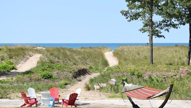 A beachside setting with a hammock, red and white Adirondack chairs, and a table with a cooler. - Lake Michigan Beach Cottages (Michigan City)