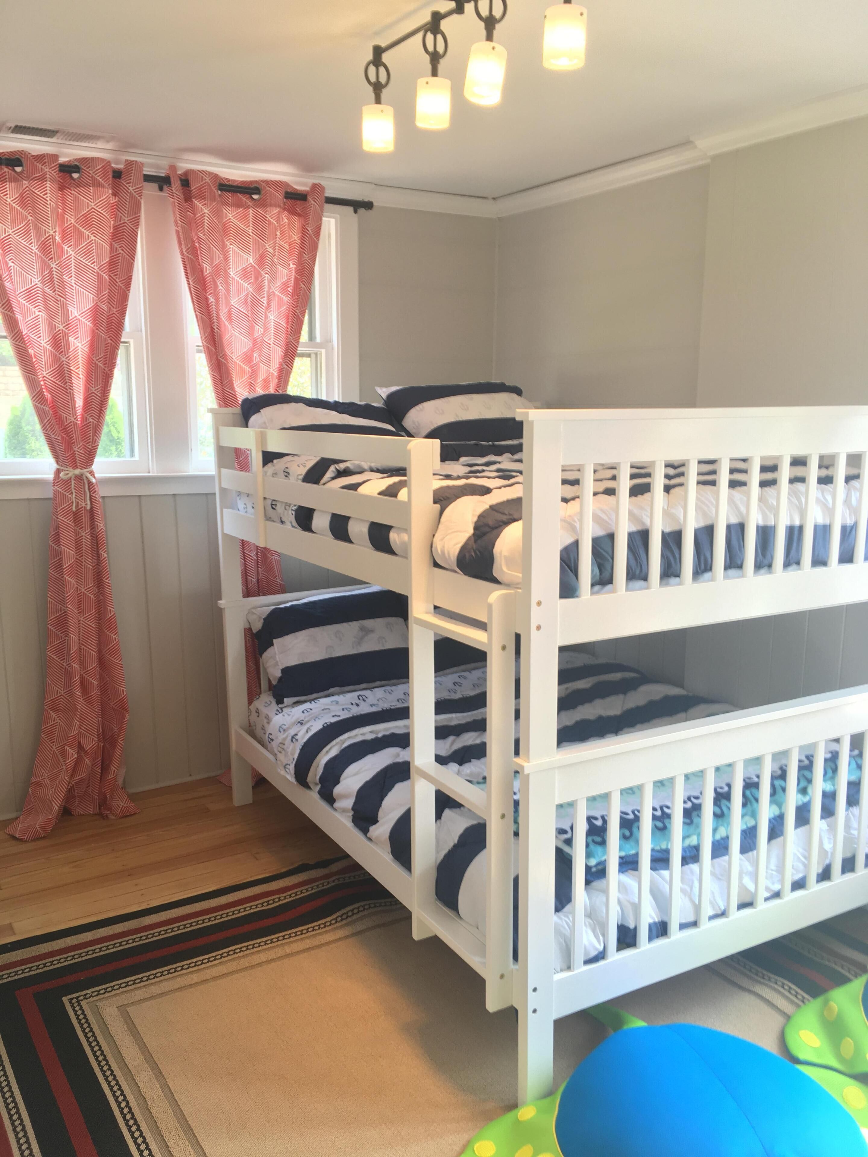A bunk bed room with a window, curtains, and a ceiling light fixture.