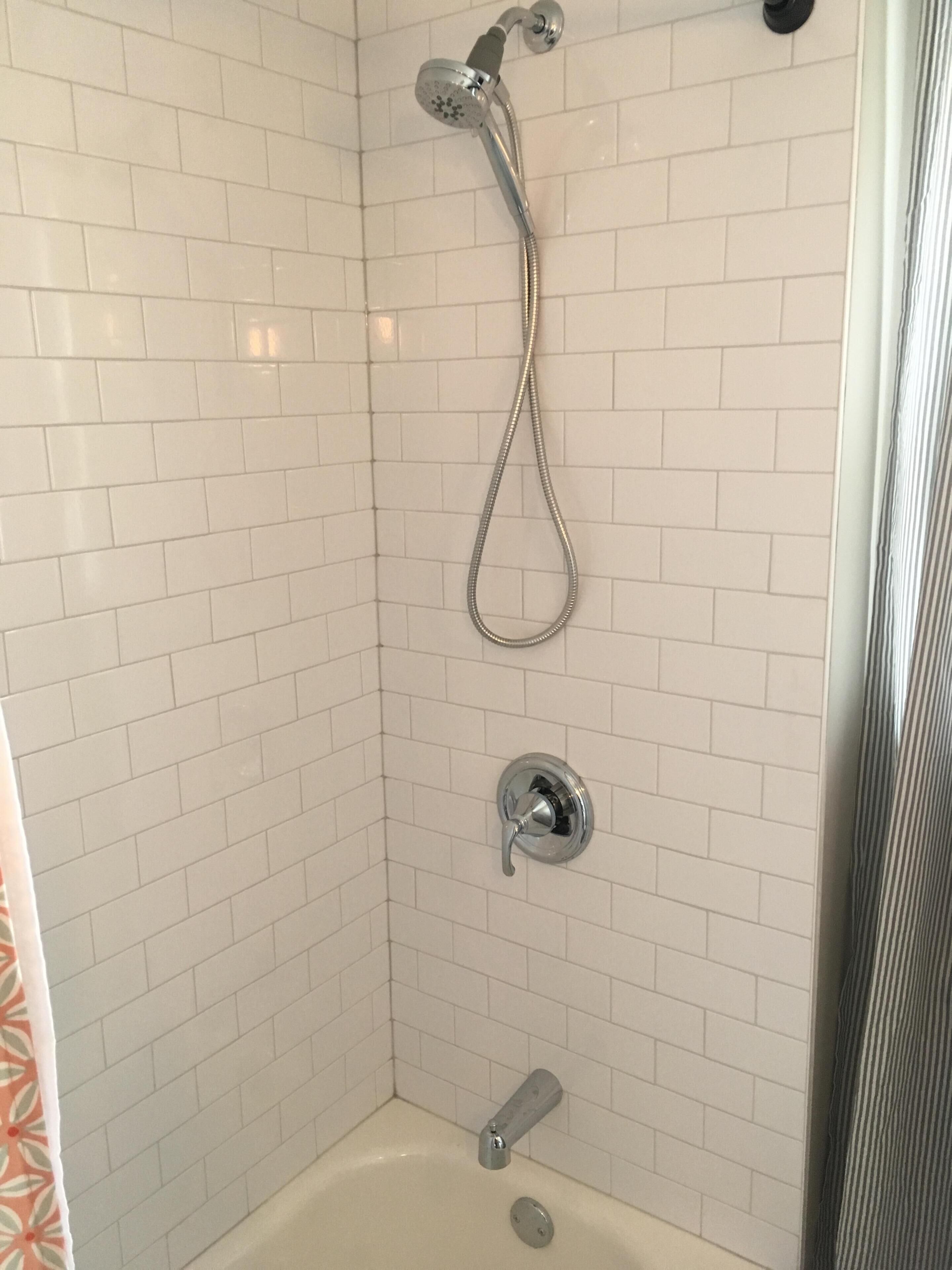 Un espacio de ducha con paredes de azulejos blancos y una bañera.