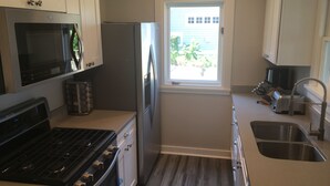 A compact kitchen with a stove, oven, microwave, refrigerator, and a window providing natural light. - Lake Michigan Beach Cottages (Michigan City)