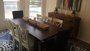 A dining area with a wooden table, white chairs, candle holders, a chandelier, and a colorful abstract painting on the wall. - Lake Michigan Beach Cottages (Michigan City)