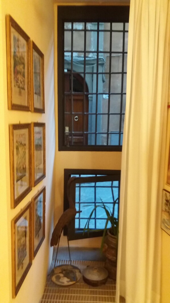 A narrow hallway with a window and a door, framed pictures on the wall, and a pet bed with a bowl.