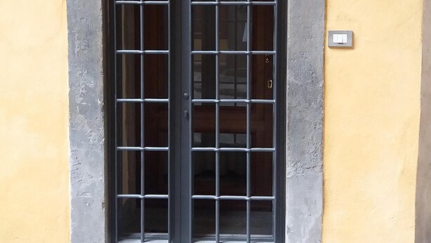 A door with a metal grid design, a small light switch, and a number plaque on the wall. - Michelangelo's retreat, a small residence on the ground floor of a  (Firenze)