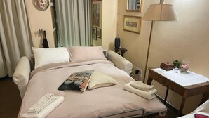 A hotel room with a bed, bedside table, lamp, and a small table with a vase. - Michelangelo's retreat, a small residence on the ground floor of a  (Firenze)