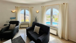 Un salon avec deux canapés noirs, une petite table et une vue sur une piscine, visible à travers de grandes fenêtres.