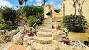 Un escalier en pierre mène à un bâtiment à la façade jaune, entouré de verdure et de plantes en pot.