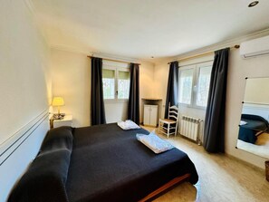 A hotel room with a bed, a desk, a chair, a radiator, and a window with curtains.