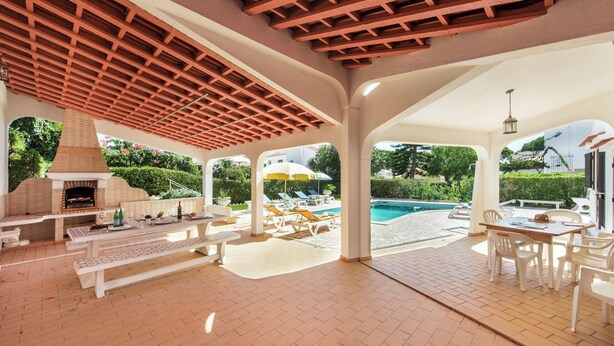 Eine Terrassengruppe im Freien mit einem Ziegel-Barbecue, weißer Möbel und einem Swimmingpool im Hintergrund.