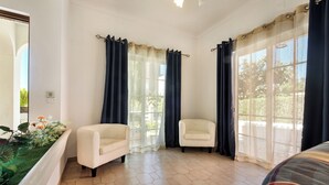 Ein Zimmer mit zwei weißen Sesseln, einem großen Fenster mit Vorhängen und einem sechseckig gefliesten Boden.