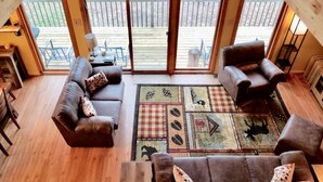 A cozy living room with a brown leather sofa, a matching armchair, and a plaid throw blanket. A wooden coffee table and a rug with various patterns are in the center. - On the Betsie River, fish off dock, close to Crystal Mountain, trails, lakes! (Thompsonville)