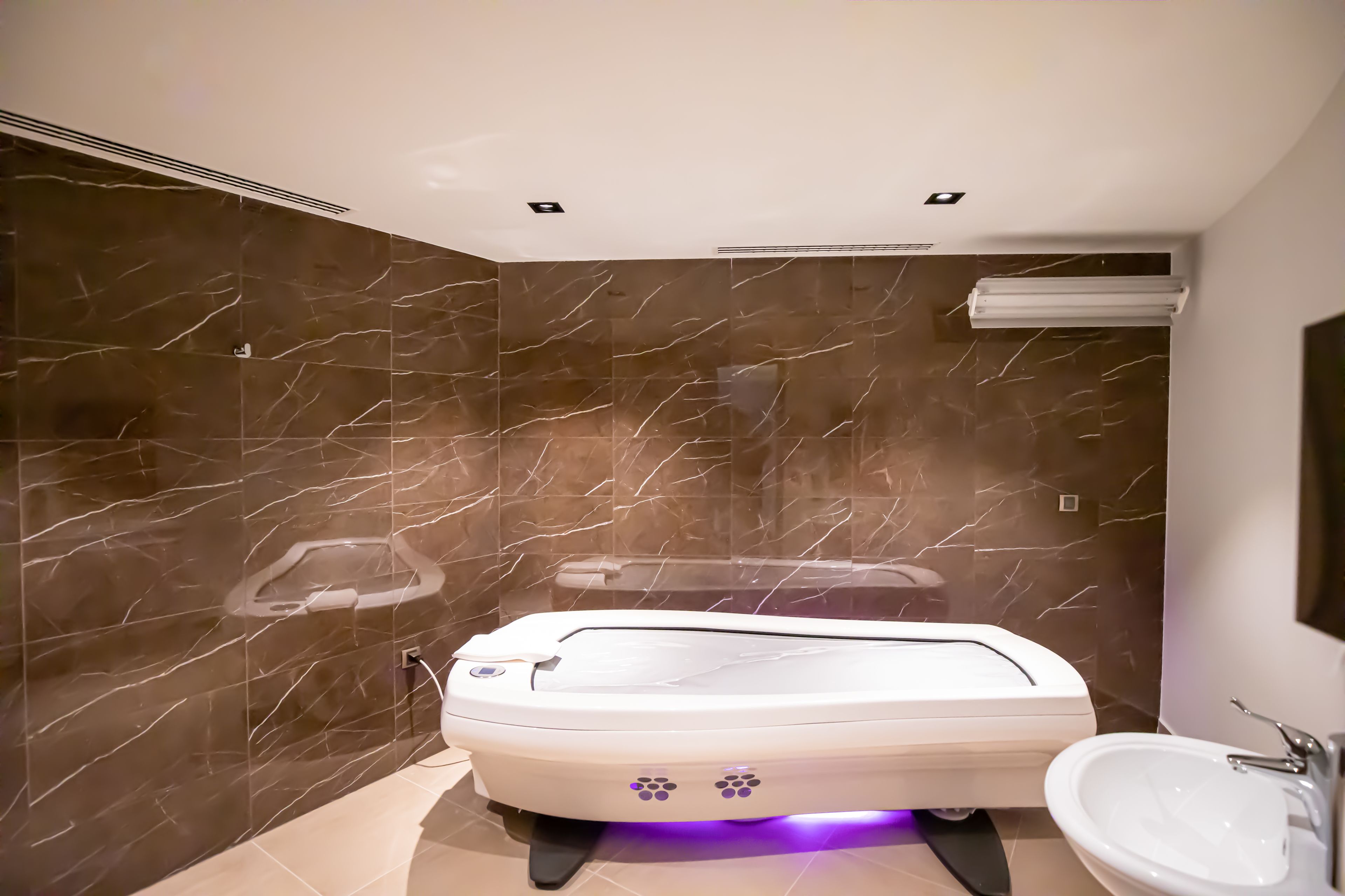 Une salle de bain moderne avec un mur en marbre, une baignoire blanche et un lavabo.