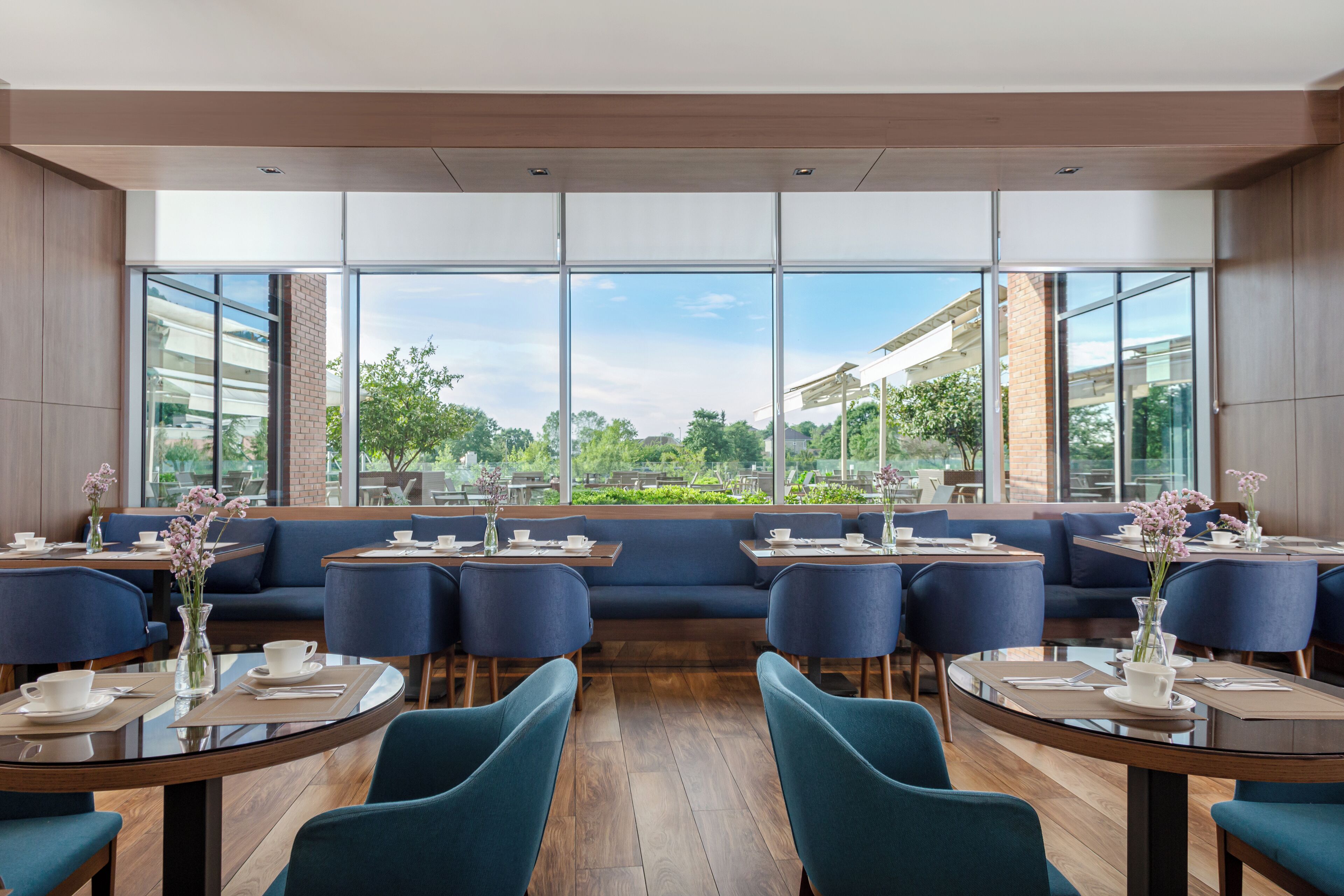 Un restaurante moderno con ventanas amplias, asientos azules y suelo de madera.
