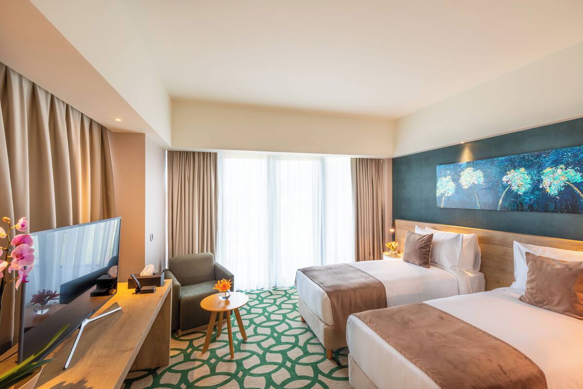 Ein Hotelzimmer mit zwei Betten, einem Schreibtisch mit Fernseher, einem kleinen Tisch mit Blumenvase und einem Bild an der Wand.