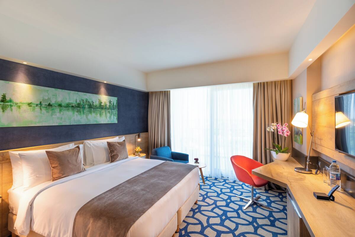 Ein Hotelzimmer mit einem großen Bett, einem Schreibtisch mit Stuhl, einem Fernseher und einem Bild an der Wand.