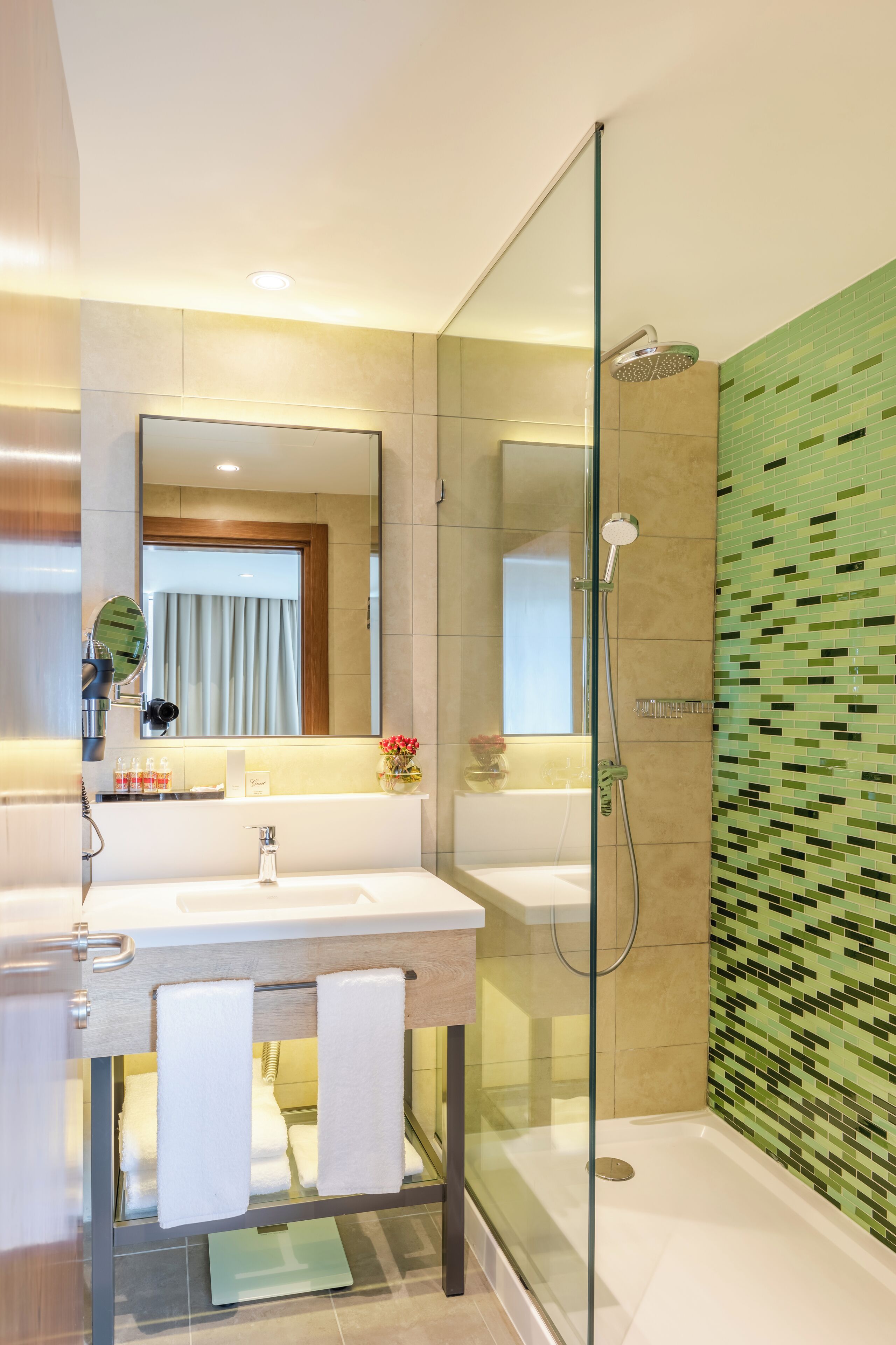 A modern bathroom with a glass-enclosed shower, a large mirror, and a tiled wall.