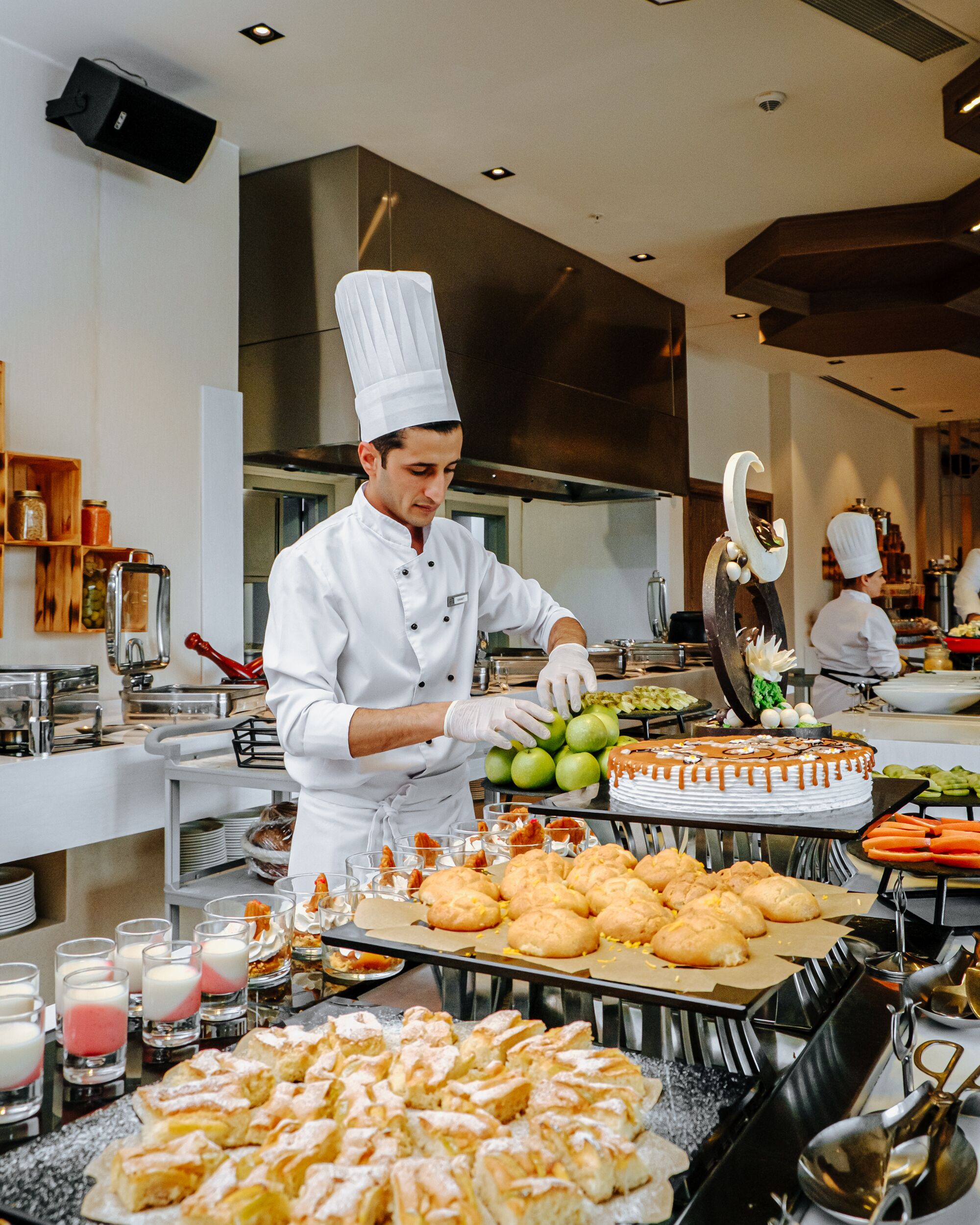 A chef in a professional kitchen preparing food, with various dishes and ingredients visible on the counter.