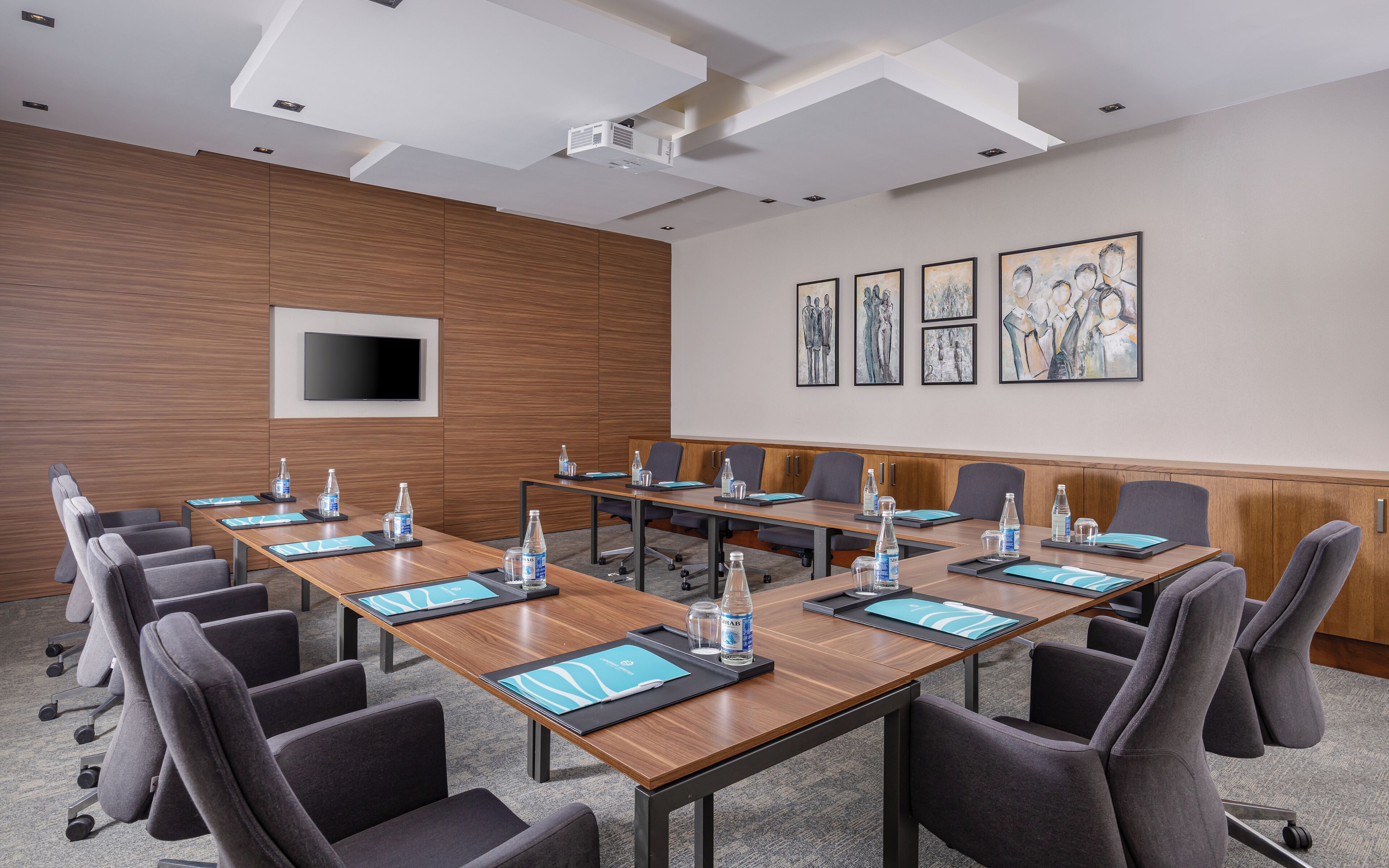 Une salle de conférence avec une longue table, des chaises, des bouteilles d’eau et un téléviseur à écran plat.