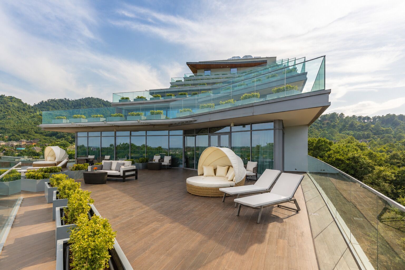 A modern rooftop with glass railings, outdoor seating, and a view of the surrounding landscape.