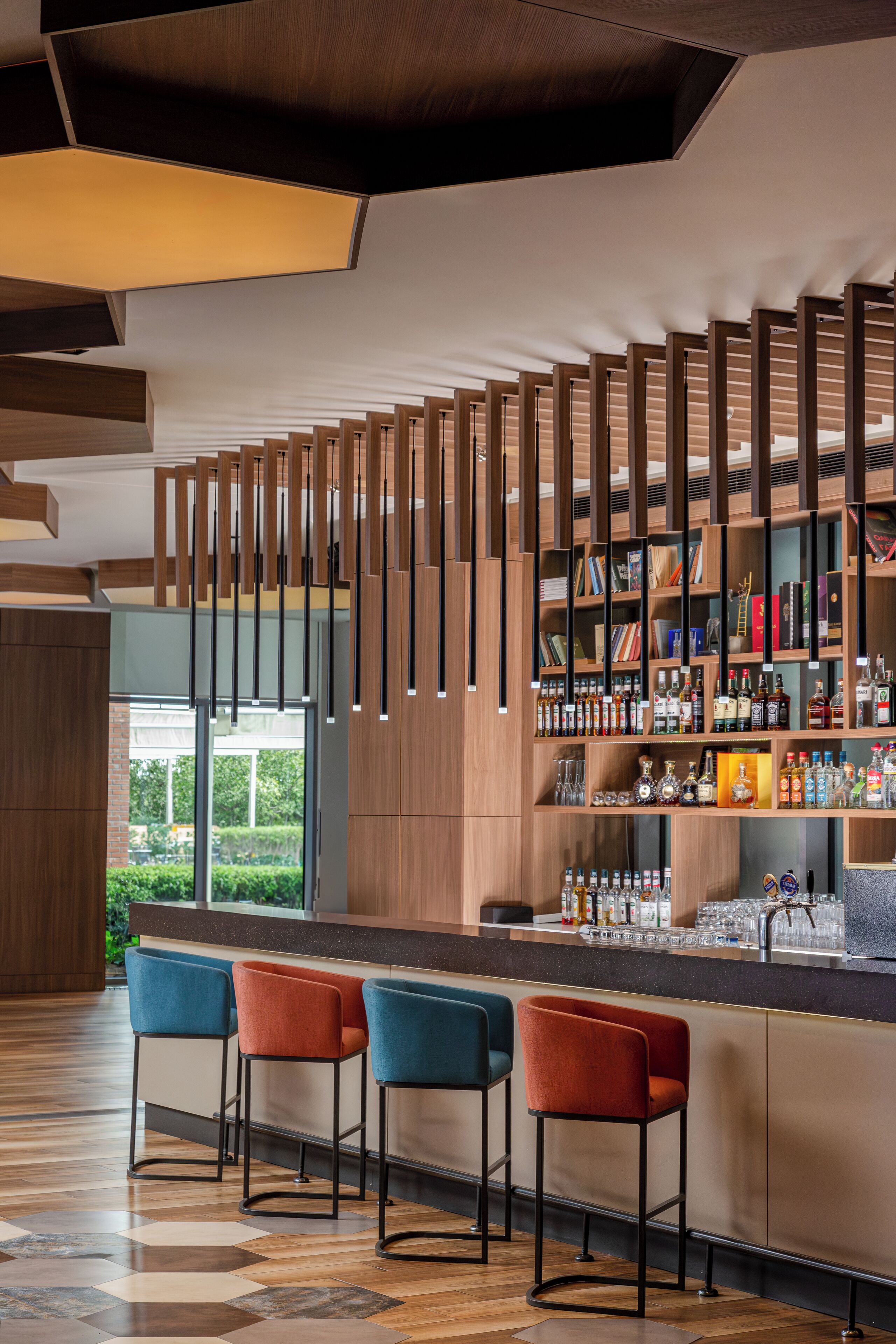 A modern bar area with wooden shelves, bar stools, and a view of greenery outside.