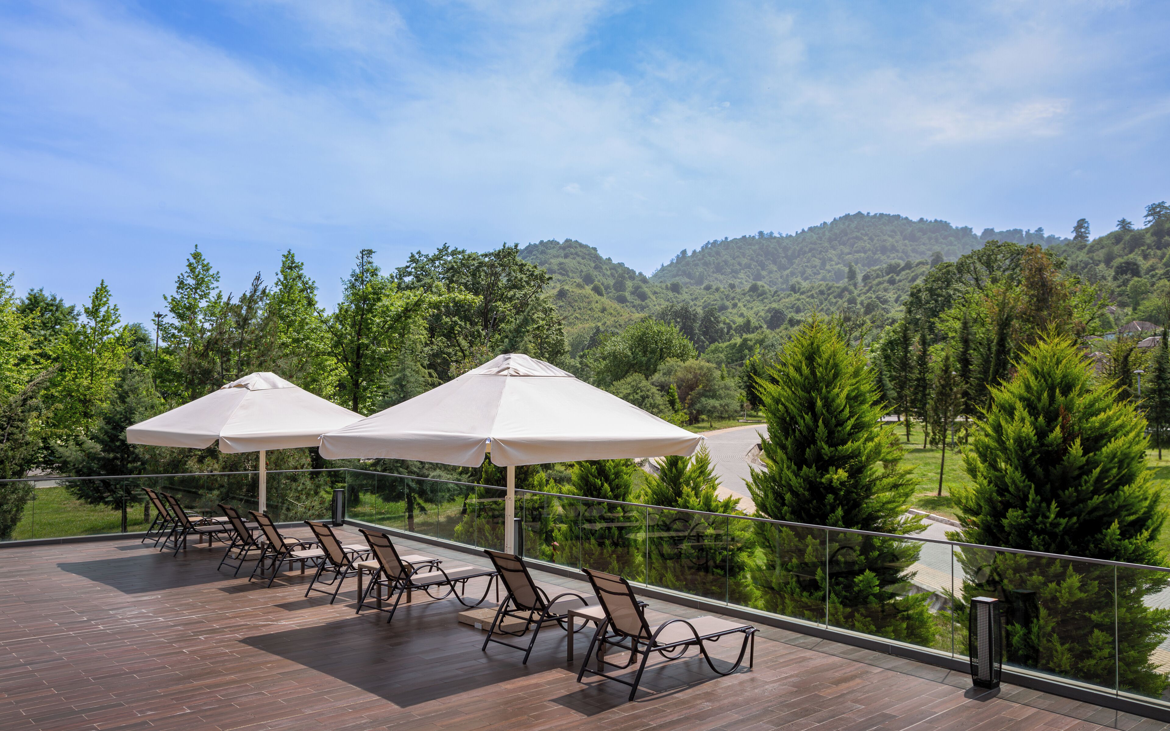 Terraza con mobiliario exterior y sombrillas, con vistas a una ladera boscosa.