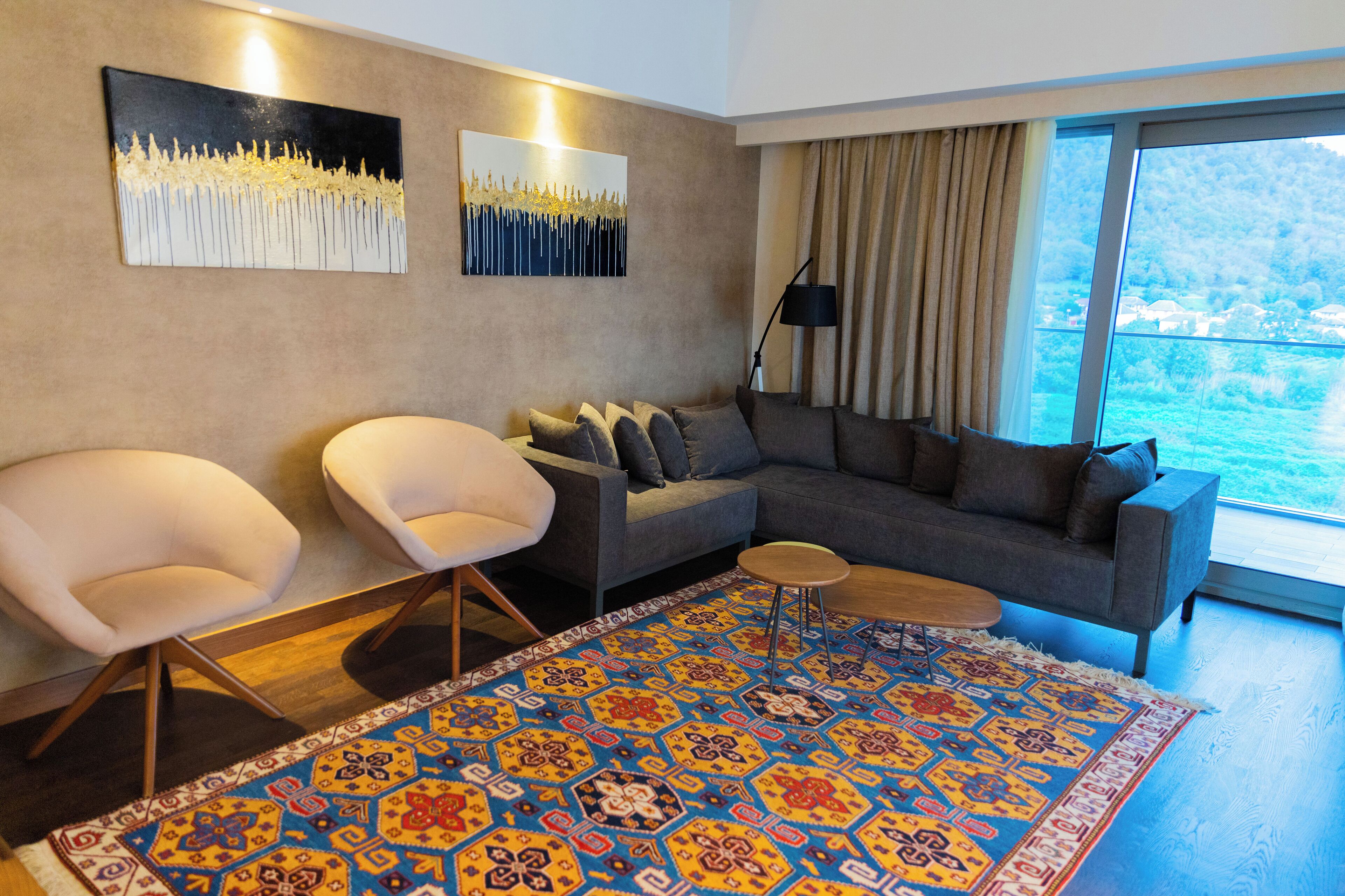 Una sala de estar moderna con un sofá gris, dos sillones blancos, un tapiz estampado y obras de arte en las paredes.