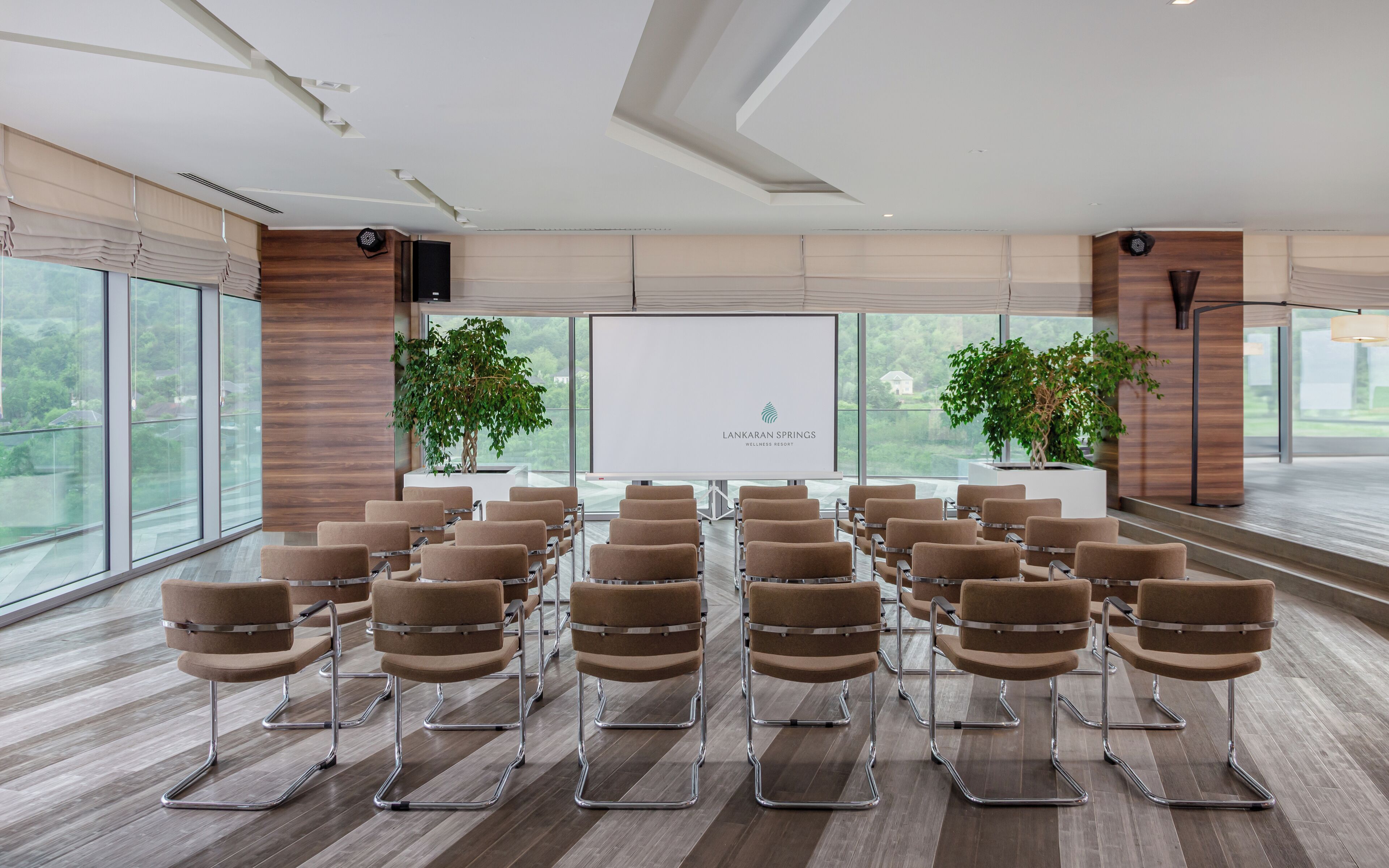A conference room with rows of chairs, a presentation screen, and potted plants.