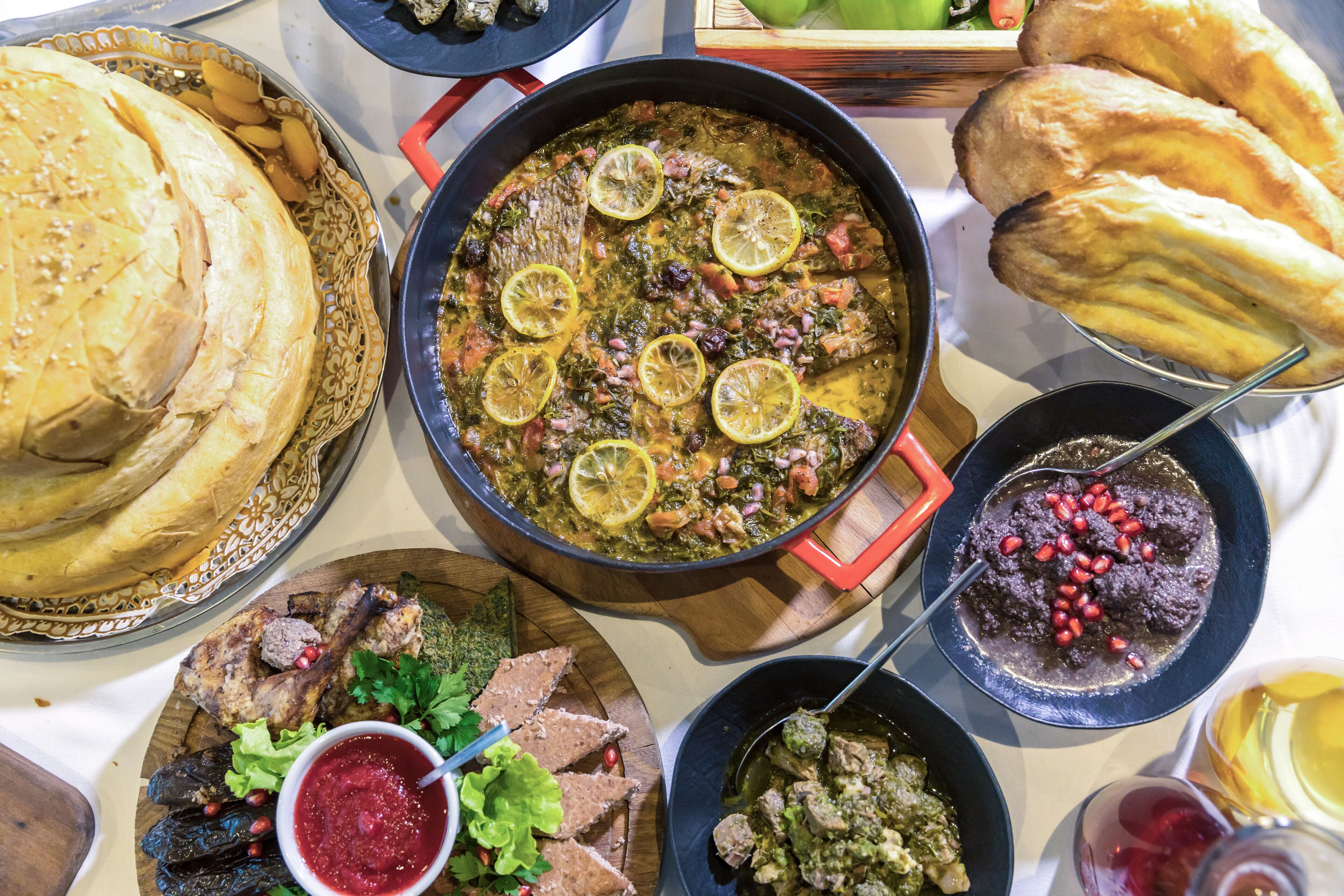 Diverse gerechten, waaronder een grote pan stoofpot, brood en andere etenswaren op een tafel.
