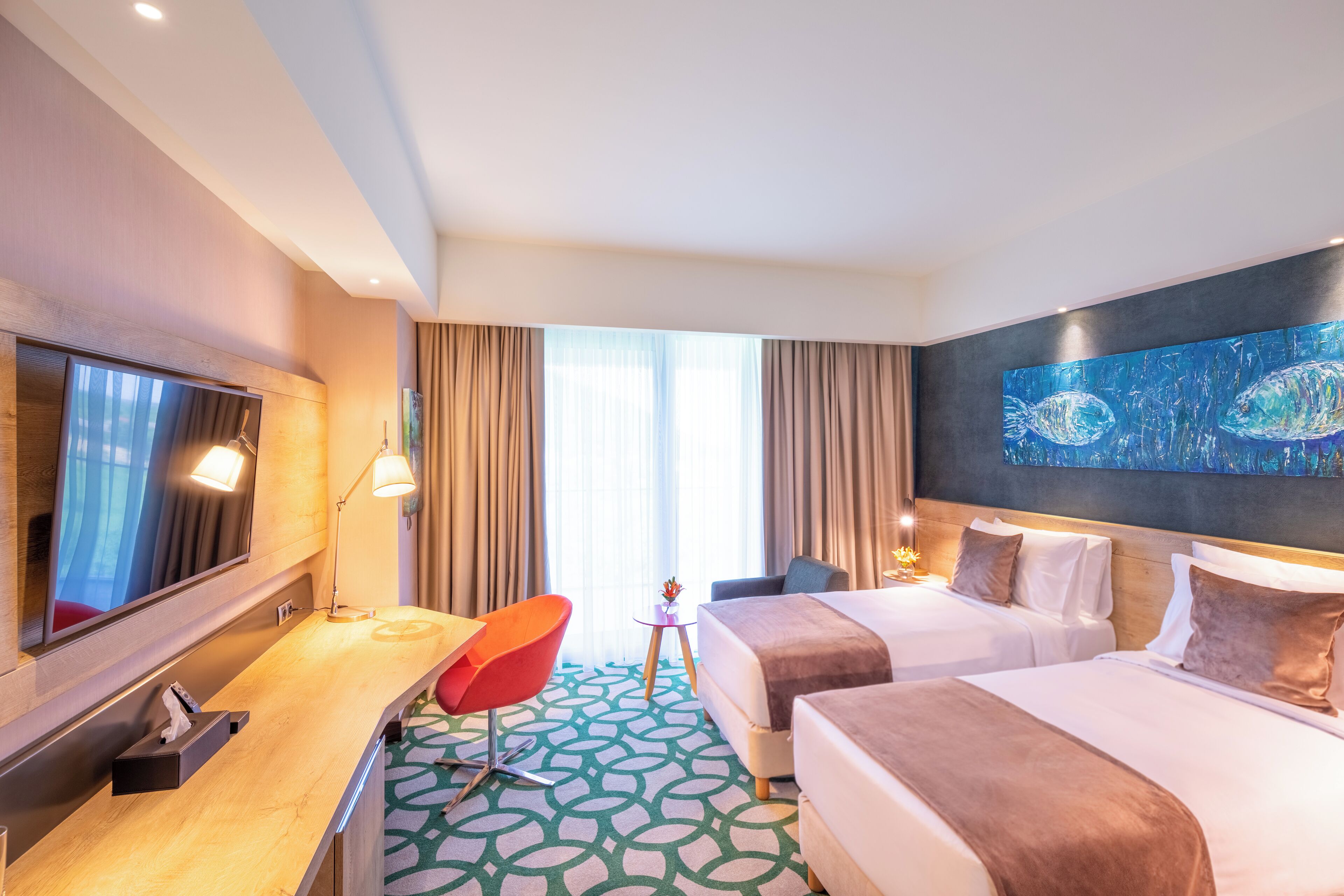 A hotel room with a large bed, a smaller bed, a desk with a chair, a TV, and a painting on the wall.