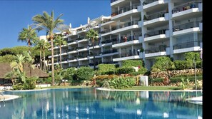 A hotel with multiple balconies, a swimming pool, and lush greenery.