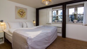 A bedroom with a large bed, a nightstand, a wall-mounted lamp, a window with curtains, and a framed picture on the wall. - Apartments Bandholm (Bandholm)