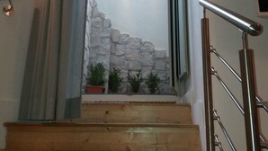 A wooden staircase with a metal handrail, leading to a stone wall with potted plants. - Munaciello Rooms (Naples)