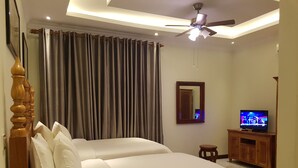 Une chambre d’hôtel avec deux lits, un ventilateur de plafond, une télévision et un miroir.