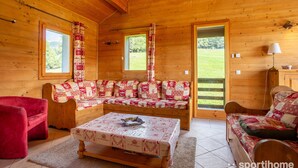 Ein gemütliches Holzhaus-Interieur mit einer Sofagarnitur, einem roten Sessel und einem Tisch mit Unterlage.