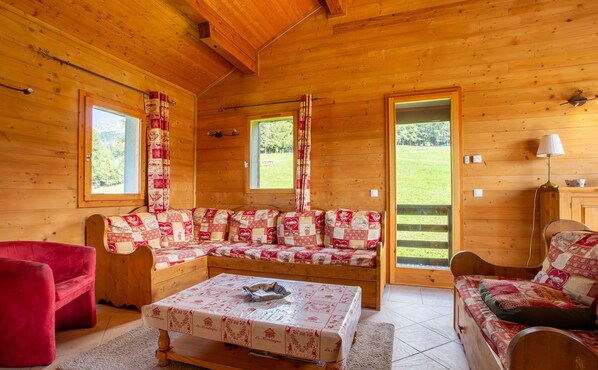 A cozy wooden cabin interior with a sofa set, a red armchair, and a table with a placemat.
