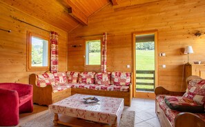 Interior acogedor de una cabaña de madera con un sofá, un sillón rojo y una mesa con un mantel individual.