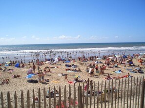 A crowded beach with people sunbathing, swimming, and walking along the shore.