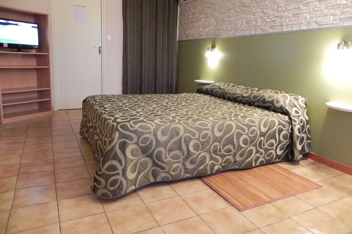 Une chambre à coucher comprenant un lit, un téléviseur, un rideau et un luminaire fixé au mur.