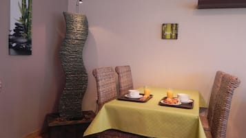 Comedor con mesa dispuesta para dos, mantel verde, sillas de mimbre y un adorno de pared.