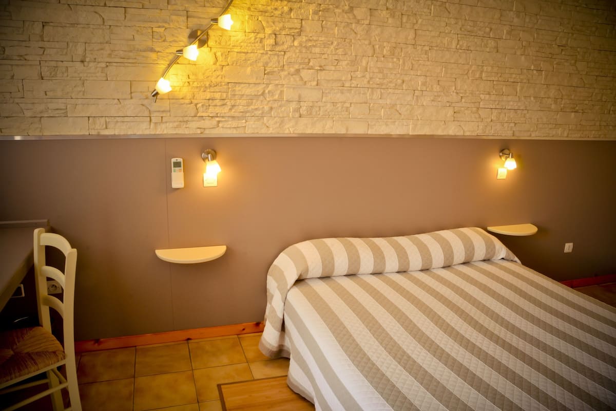 Une chambre à coucher comprenant un lit, une chaise, une étagère fixée au mur et un mur à la texture rappelant la pierre.