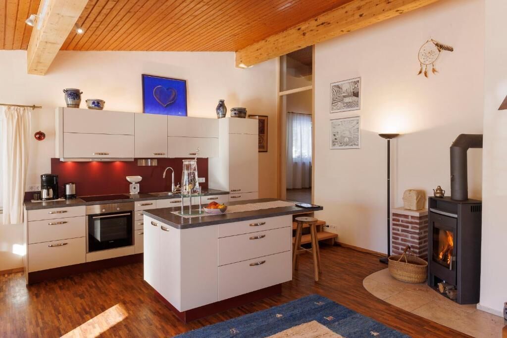 A modern kitchen with white cabinetry, a central island, and a wood-burning stove.