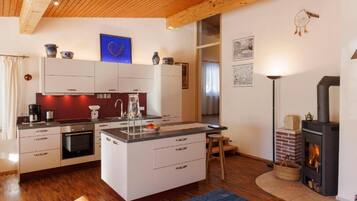 A modern kitchen with white cabinetry, a central island, and a wood-burning stove.