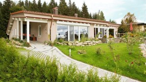 A modern house with a covered patio, a stone pathway, and a well-maintained garden. - Haus am Waldpark (Scheidegg)