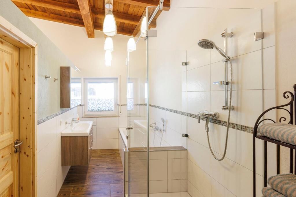 Een badkamer met een douche, wastafel en raam.